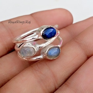 Può includere: Tre anelli d'argento con pietre preziose ovali. L'anello superiore ha una pietra blu scuro, quello centrale una pietra blu chiaro e quello inferiore una pietra blu-grigiastra. Gli anelli sono impilati. Il testo "RoyalRingsRaj" è visibile.