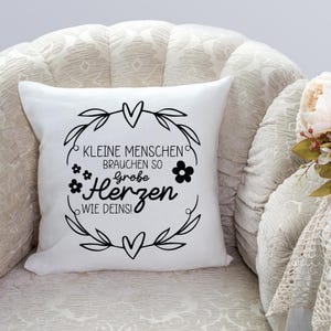Peut inclure: Un coussin blanc avec du texte noir et un motif floral. Le texte dit "Kleine Menschen brauchen so gro&szlig;e Herzen wie Deins!"