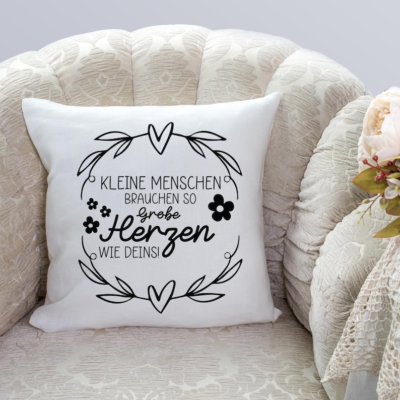 Peut inclure: Un coussin blanc avec du texte noir et un motif floral. Le texte dit "Kleine Menschen brauchen so gro&szlig;e Herzen wie Deins!"
