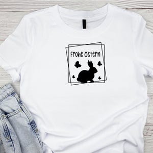 May include: White t-shirt with a black silhouette of a rabbit and the text "Frohe Ostern" inside a black square frame.