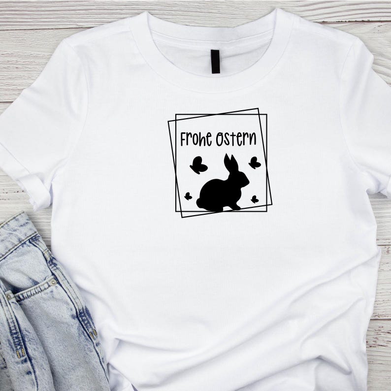 May include: White t-shirt with a black silhouette of a rabbit and the text "Frohe Ostern" inside a black square frame.