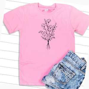 May include: A pink t-shirt with a black line drawing of a bouquet of flowers on the front.