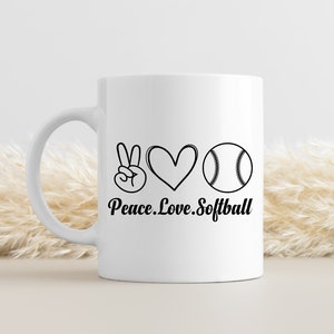 May include: White ceramic coffee mug with a black peace sign, heart, and softball graphic. The text "Peace. Love. Softball" is printed below the graphic.