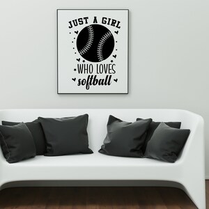 May include: A black and white graphic print with the text "Just a girl who loves softball" and a softball graphic. The graphic is framed and hanging on a white wall above a white couch.