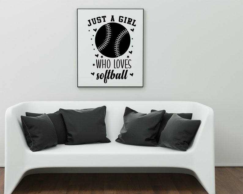 May include: A black and white graphic print with the text "Just a girl who loves softball" and a softball graphic. The graphic is framed and hanging on a white wall above a white couch.