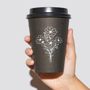May include: A black to-go coffee cup with a white floral design. The design features a bouquet of stylized flowers.