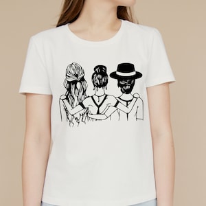 May include: A white t-shirt with a black graphic of three women standing back to back with their arms around each other. The woman in the middle has her hair pulled back in a bun. The woman on the left has long, flowing hair. The woman on the right is wearing a hat.