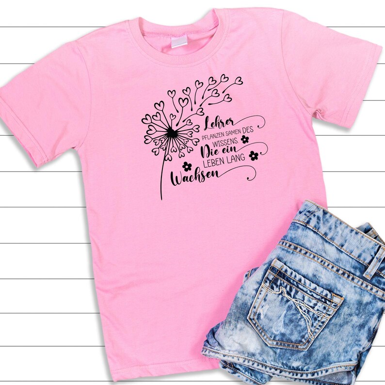 Peut inclure: T-shirt rose avec un motif de pissenlit noir et le texte "Lehrer Pflanzen Samen des Wissens Die ein Leben Lang Wachsen".