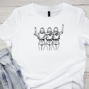 May include: A white t-shirt with a black line drawing of three women standing back to back with their arms around each other. The women are wearing denim shorts and have long hair.