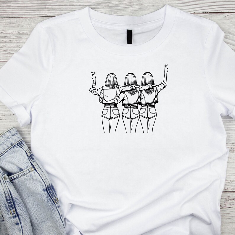 May include: A white t-shirt with a black line drawing of three women standing back to back with their arms around each other. The women are wearing denim shorts and have long hair.