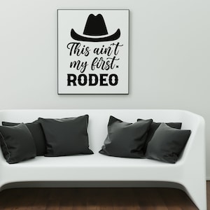 以下が含まれることがあります： カウボーイハットと「This ain't my first rodeo」というテキストが書かれた白黒のグラフィックプリントです。