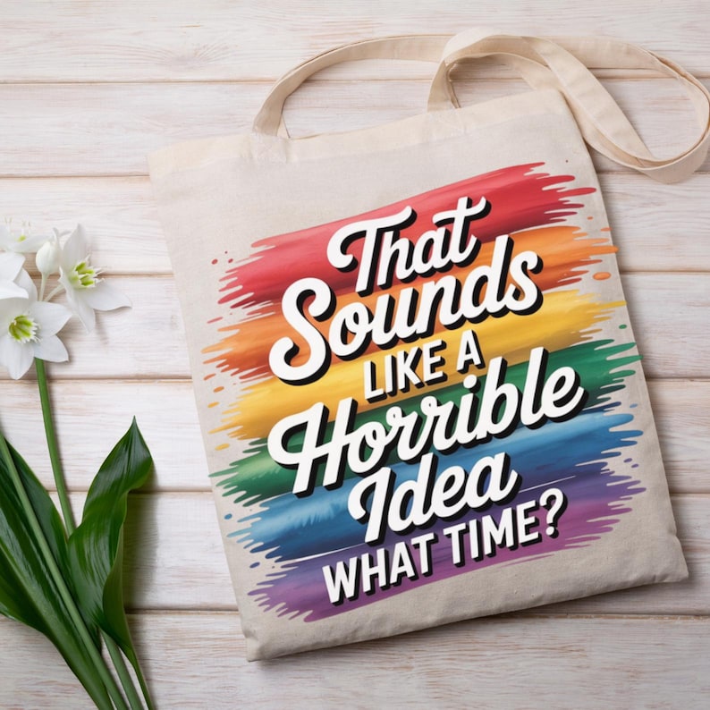 May include: Beige canvas tote bag with the text "That Sounds Like a Horrible Idea WHAT TIME?" in white, outlined in black, over a rainbow-colored brushstroke design. The bag has a simple, neutral design with long handles.