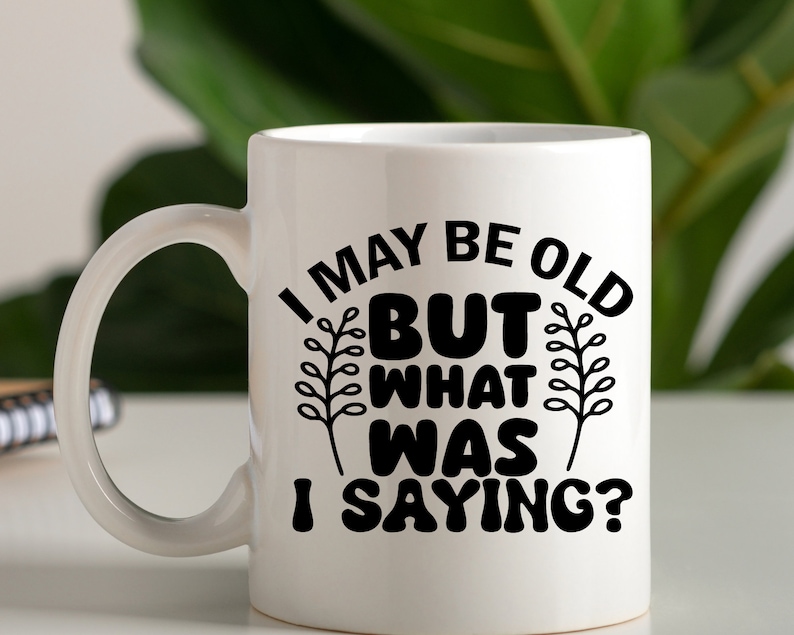 May include: White ceramic mug with a black design that reads "I may be old but what was I saying?" The design includes two stylized plant sprigs.