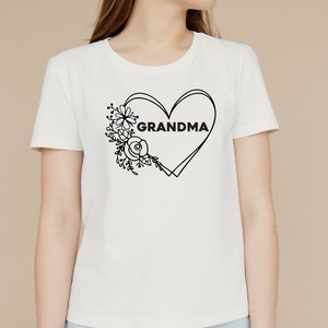 May include: White t-shirt with a black outline of a heart with the word "GRANDMA" inside. The heart is surrounded by a floral design.