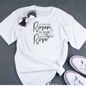 Op de afbeelding: Wit T-shirt met zwarte tekst die "Ich m&ouml;chte keine Rosen, ich nehme lieber einen Rose" zegt.
