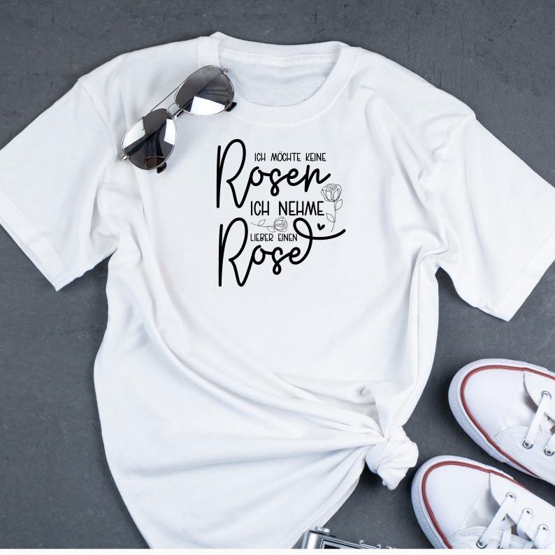 Op de afbeelding: Wit T-shirt met zwarte tekst die "Ich m&ouml;chte keine Rosen, ich nehme lieber einen Rose" zegt.