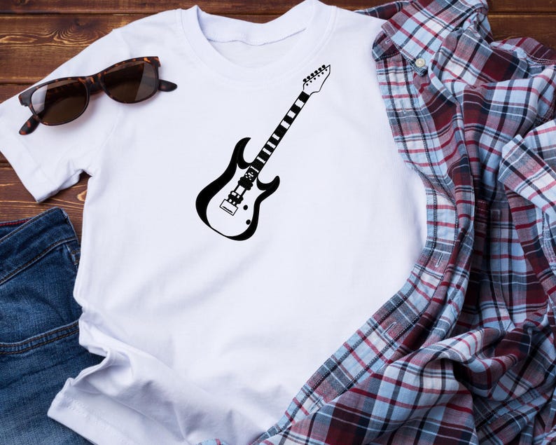 May include: White t-shirt featuring a black electric guitar graphic. The guitar design is a simple outline. Sunglasses and a plaid shirt are also visible in the image. The shirt is made of a soft material.