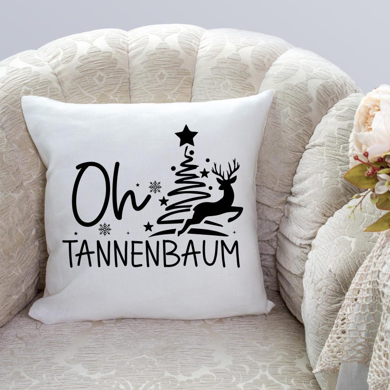 May include: White throw pillow with black text and a graphic of a Christmas tree and a deer. The text reads "Oh Tannenbaum".