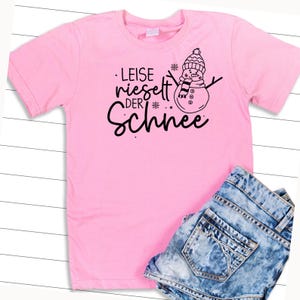 May include: Pink t-shirt with a black graphic of a snowman and the text "Leise rieselt der Schnee".