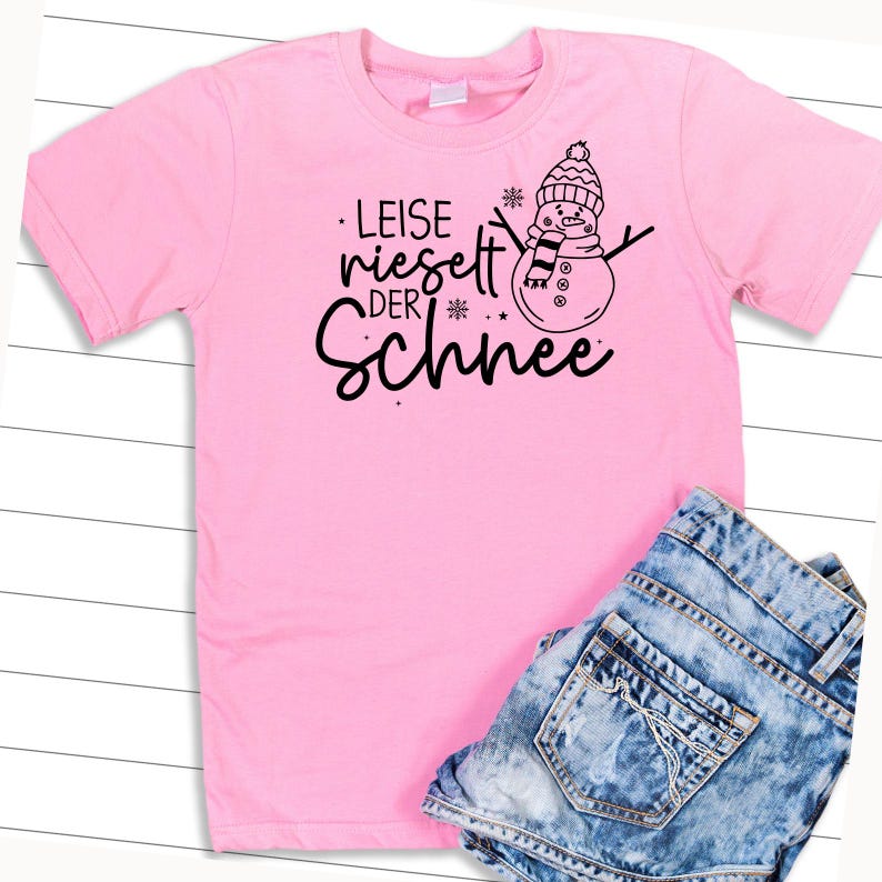 May include: Pink t-shirt with a black graphic of a snowman and the text "Leise rieselt der Schnee".