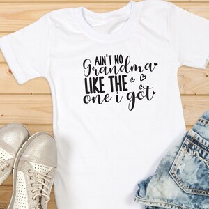 May include: White t-shirt with the text "Ain't no grandma like the one I got" in black lettering with three small hearts.