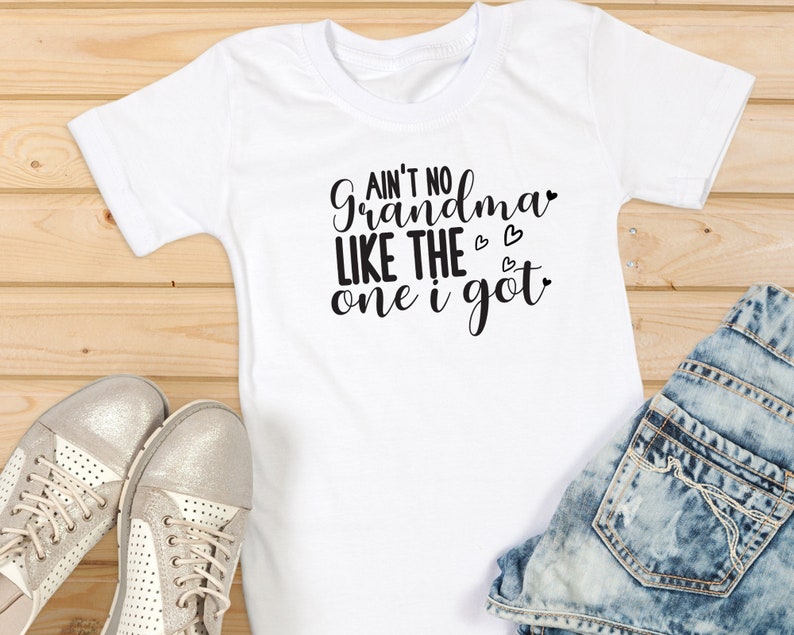 May include: White t-shirt with the text "Ain't no grandma like the one I got" in black lettering with three small hearts.