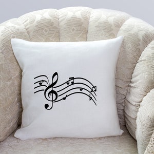 May include: White throw pillow with a black musical note design. The design features a treble clef and musical notes on a wavy line.