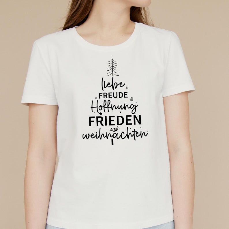 May include: White t-shirt with a black Christmas tree design. The tree is made up of the words "liebe", "freude", "hoffnung", "frieden", and "weihnachten".