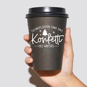 May include: A black to-go coffee cup with white text that reads "Schneeflocken sind das Konfetti - des Winters" which translates to "Snowflakes are the confetti of winter".