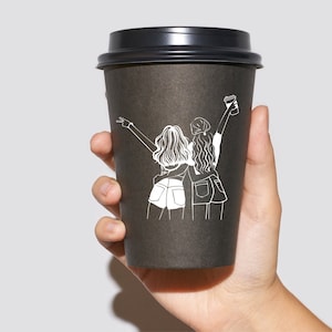 May include: Black to-go coffee cup with a white line drawing of two women holding hands and smiling. The women are wearing casual clothing and have long hair.
