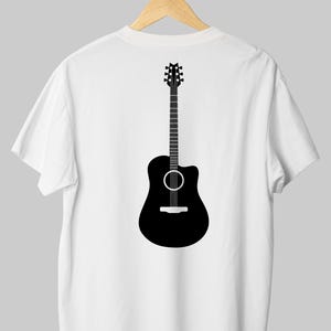 May include: White t-shirt with a black acoustic guitar graphic on the back. The guitar illustration features a detailed neck, sound hole, and body shape. The shirt is hanging on a wooden hanger.