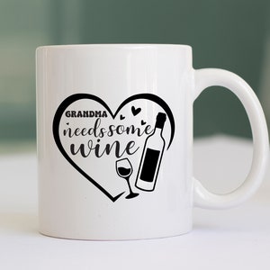 May include: White ceramic mug with a black heart design that says "Grandma needs some wine" with a wine bottle and glass inside the heart.