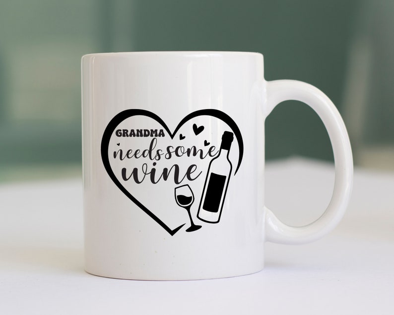 May include: White ceramic mug with a black heart design that says "Grandma needs some wine" with a wine bottle and glass inside the heart.