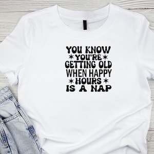 May include: White t-shirt with black text that reads "YOU KNOW *YOU'RE* GETTING OLD WHEN HAPPY *HOURS* IS A NAP"