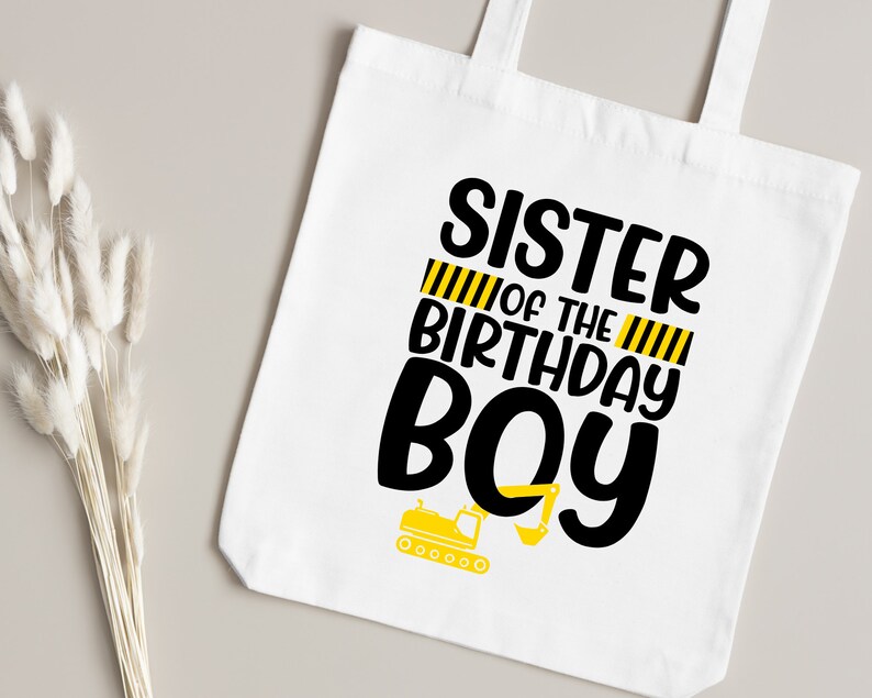 May include: White tote bag with black text that reads "Sister of the Birthday Boy" with yellow and black construction stripes and a small yellow construction vehicle graphic.