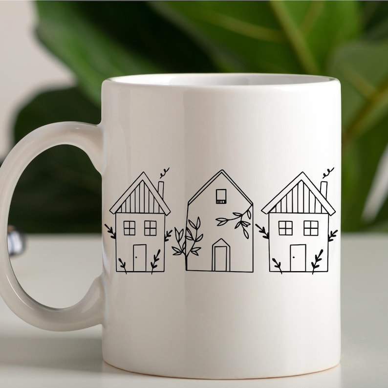 May include: White ceramic mug with a black line drawing of three houses with small trees and windows.