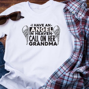 May include: White t-shirt with black text that reads "I have an angel in heaven. Call on her grandma." with a pair of angel wings on either side of the text.