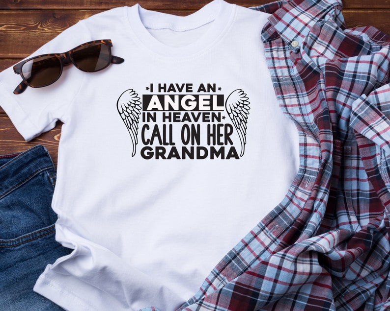 May include: White t-shirt with black text that reads "I have an angel in heaven. Call on her grandma." with a pair of angel wings on either side of the text.