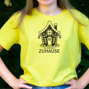 May include: A yellow t-shirt with a black gingerbread house graphic and the text "Willkommen Zuhause".