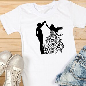 May include: White t-shirt with a black silhouette of a couple dancing. The woman is wearing a floral patterned dress.