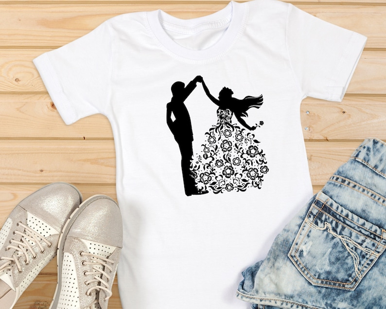 May include: White t-shirt with a black silhouette of a couple dancing. The woman is wearing a floral patterned dress.