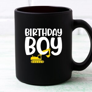 May include: Black ceramic coffee mug with a white design that says "Birthday Boy" and a yellow excavator illustration.