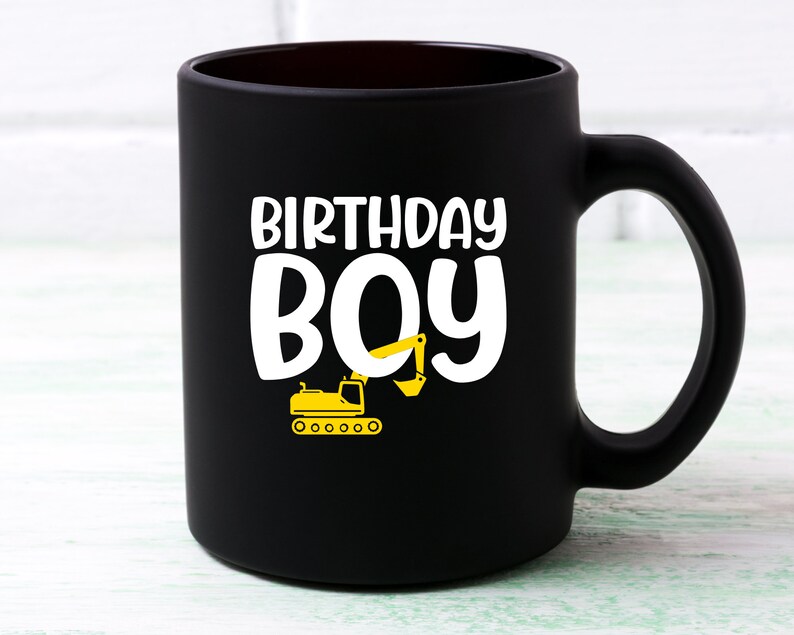 May include: Black ceramic coffee mug with a white design that says "Birthday Boy" and a yellow excavator illustration.