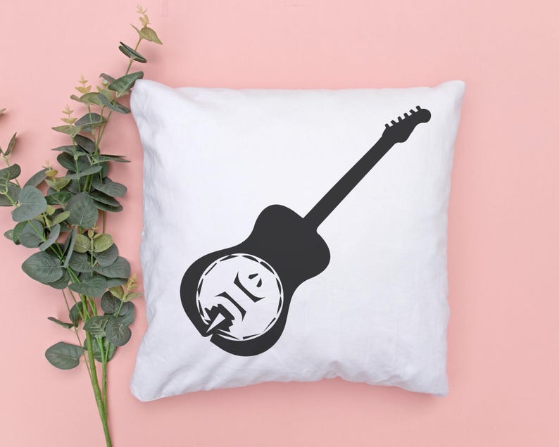 May include: White square pillow with a black guitar silhouette design. The guitar has a unique circular design on the body. The pillow is on a pink surface with green leafy branches in the corner.
