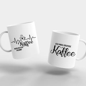 May include: Two white ceramic coffee mugs. One mug features a black graphic of a coffee cup with a heartbeat line and the text "Kaffee" and "MEIN BESTER FREUND". The other mug has the text "ICH MAG GROSSE Kaffee".