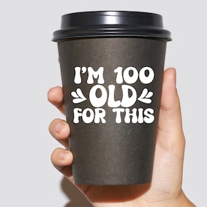 May include: A black to-go coffee cup with a white graphic that reads "I'm 100 Old For This".