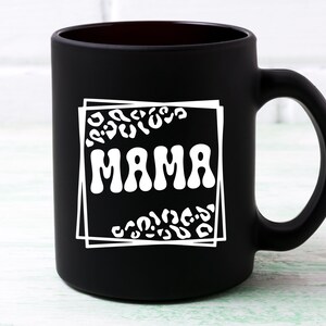 May include: Black ceramic coffee mug with a white design of a leopard print frame around the word "MAMA" in a retro font.