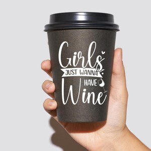 Op de afbeelding: Een zwarte koffiebeker om mee te nemen met de tekst "Girls Just Wanna Have Wine" in witte letters. Naast het woord "Wine" staat een klein wijnglasicoon.