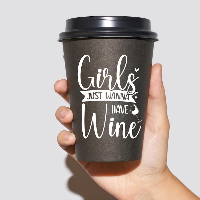 Op de afbeelding: Een zwarte koffiebeker om mee te nemen met de tekst "Girls Just Wanna Have Wine" in witte letters. Naast het woord "Wine" staat een klein wijnglasicoon.