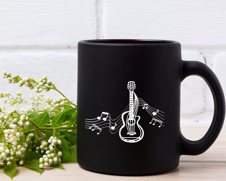 May include: Black coffee mug with a white outline of a guitar and musical notes. The mug is on a white brick background.